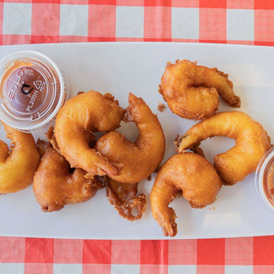 Golden-brown fried shrimp arranged on a plate with dipping sauce, set against a red-and-white checkered tablecloth.